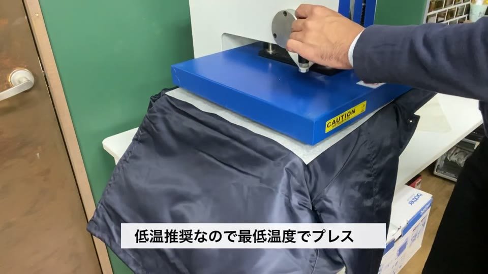 青い熱プレス機の台にジャケットをのせてプレスする様子と、低温推奨なので最低温度でプレスというテロップ