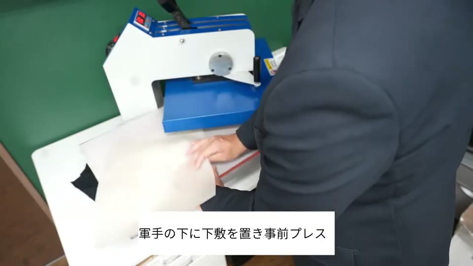 プレス機の下ゴテに下敷きを置き、軍手をのせて事前プレスしている様子