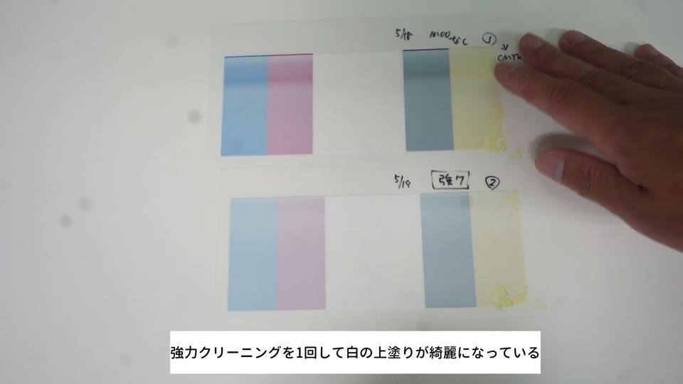 CMYKのベタの上に白を重ねたテスト印刷2枚を並べ、強力クリーニング前後で白の乗り方を比べている様子
