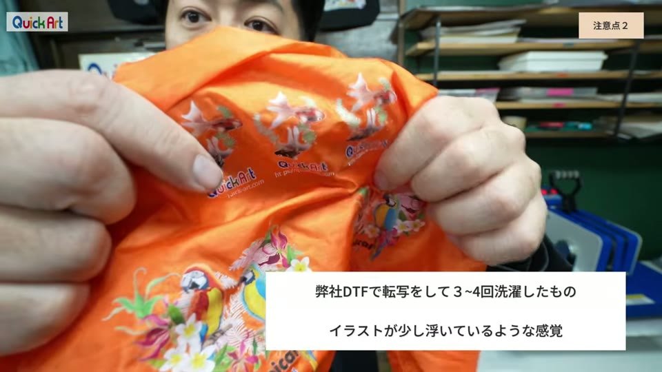 オレンジのナイロン生地にDTFでプリントした鳥のイラストを手で広げて見せている様子。弊社DTFで転写をして3〜4回洗濯したもの、イラストが少し浮いているような感覚というテロップ