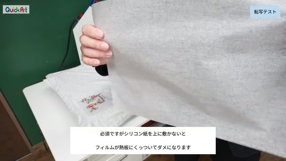 フィルムを置いたTシャツの上にシリコン紙をかぶせる様子。必須ですがシリコン紙を上に敷かないとフィルムが熱板にくっついてダメになりますというテロップ