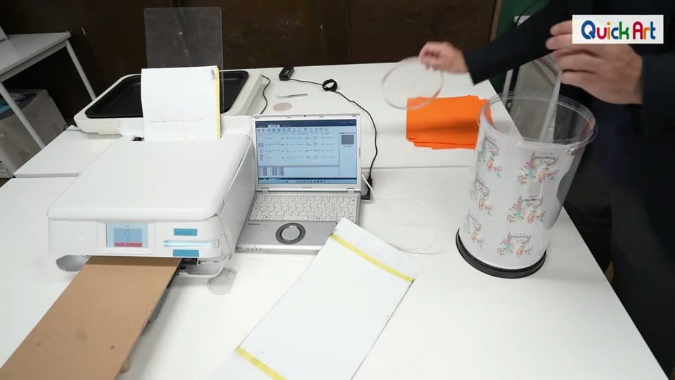 印刷を終えたフィルムを円筒形のパウダーケースに入れ、パウダーをかけている様子。後ろでプリンターが次のフィルムを印刷している