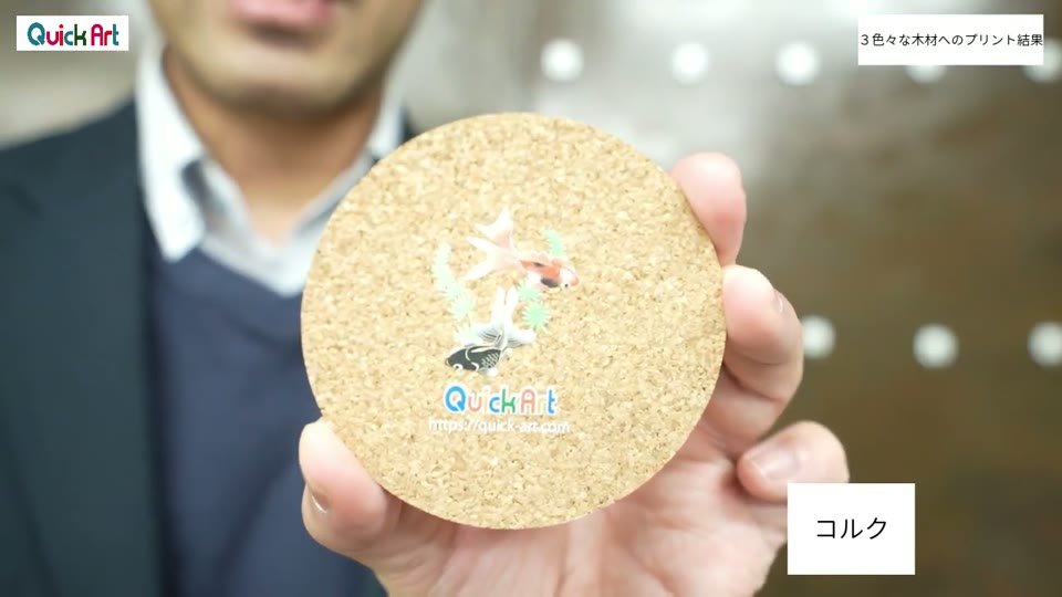 丸いコルクのコースターに、金魚のイラストとQuickArtの文字がプリントされている様子