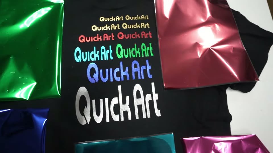 黒いTシャツにQuickArtのロゴを金・銀・赤・ピンク・青・スカイブルー・緑のメタリックホイルでプリントした見本と、各色のホイル