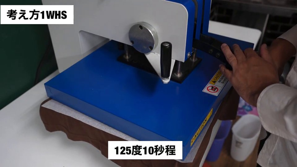 茶色のTシャツに写真の転写紙を置き、シリコン紙をかぶせてスウィング式プレス機でプレスしている様子