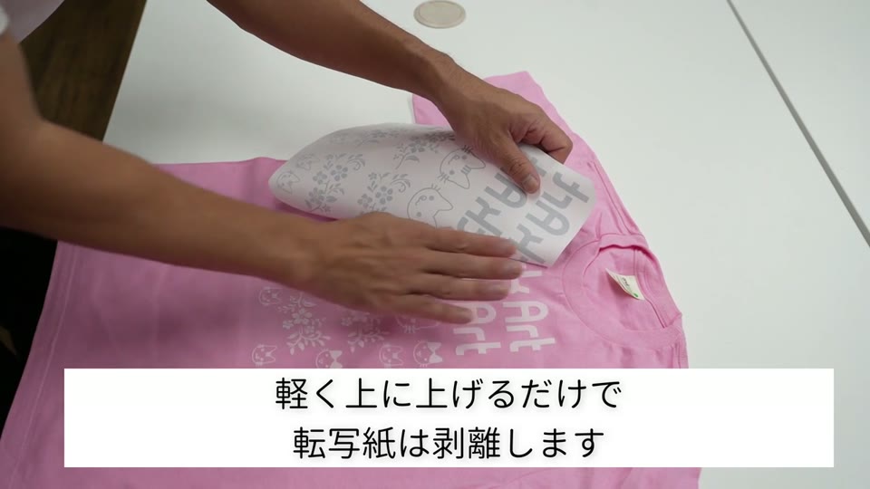 ピンクのTシャツから、転写した後の普通紙を両手で剥がしているところ