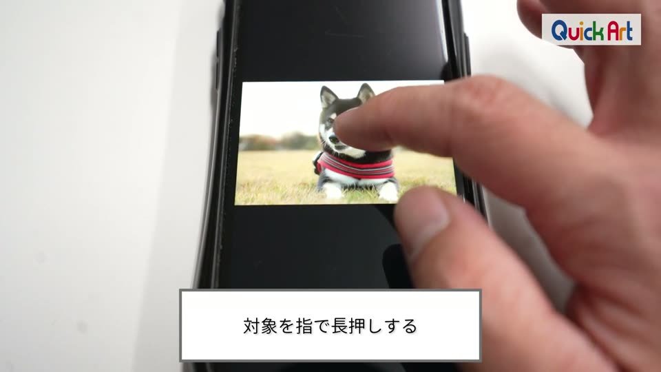 iPhoneに表示した芝生の上の柴犬の写真を、指で長押ししている様子と、対象を指で長押しするというテロップ
