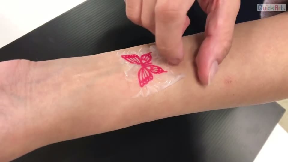 腕に貼ったちょうちょの上から、乾いてシワが寄った表面の膜を指でゆっくり剥がしているところ