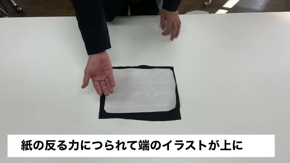 黒い生地の上に転写紙を上にして置いて冷ましている様子と、紙の反る力につられて端のイラストが上にと字幕が出ている様子