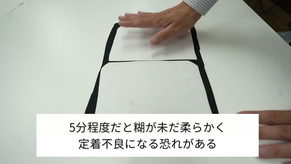黒い生地の上の転写紙を手で押さえている。テロップは5分程度だと糊が未だ柔らかく定着不良になる恐れがある