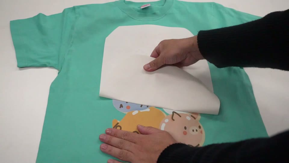 ミントグリーンのTシャツにプレスした転写マークの裏紙を、完全に冷めてから剥がしている様子