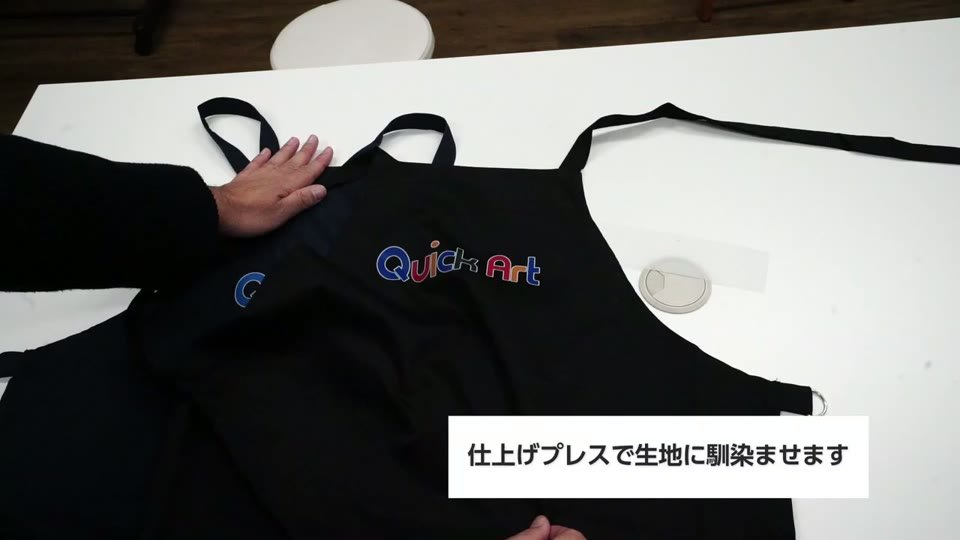 紺のエプロンにプリントしたQuick Artのロゴの上にフォースインペーパーSを乗せて仕上げプレスする様子