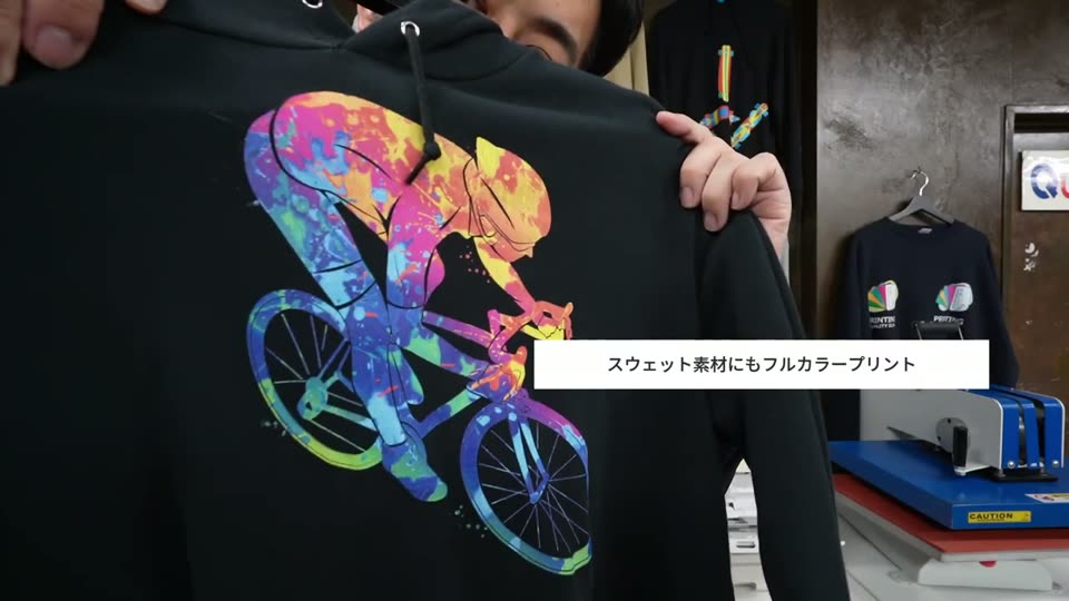 黒いスウェットパーカーの背中にプリントした、カラフルな自転車に乗る人のイラスト