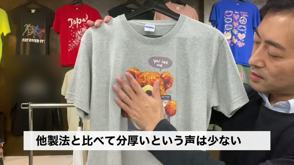 グレーのTシャツのクマのイラストを手のひらで触り、「他製法と比べて分厚いという声は少ない」とテロップが出ている場面