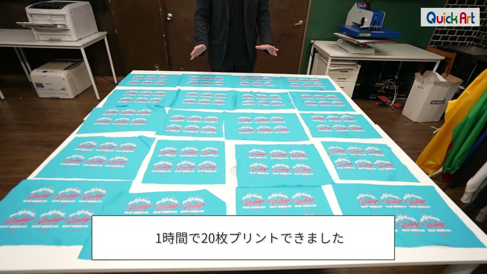 作業台いっぱいに並べた、プリントを終えた水色の生地20枚。1時間で20枚プリントできましたというテロップ